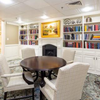 A cozy library room with a round table and chairs surrounded by bookshelves and artwork.