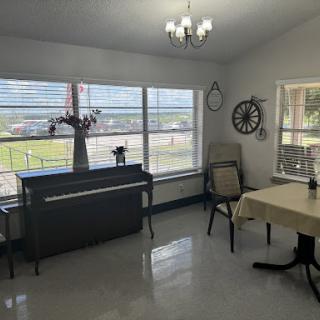 A bright and spacious room featuring a piano, dining table, and large windows.