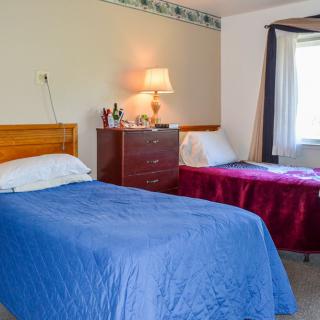 A cozy bedroom with two beds, featuring blue and red bedspreads, a nightstand with a lamp, and a window for natural light.