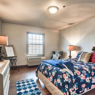 A cozy bedroom interior with floral bedding, two lamps, and a window illuminating the space.