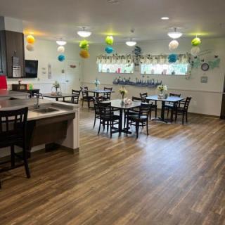 A decorated dining area with tables and chairs, featuring colorful balloons and wood flooring.