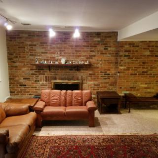 A cozy living room with a brick accent wall, featuring a fireplace, leather sofas, and a decorative carpet.