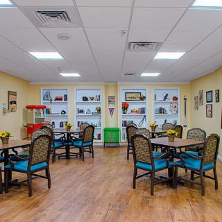 A brightly lit seating area with several tables and chairs, decorated with various wall hangings and a popcorn machine.