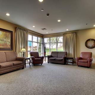 A cozy living room with sofas and armchairs, featuring large windows and warm lighting.
