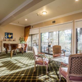 A cozy living room with large windows letting in natural light, featuring elegant furniture and a patterned carpet.