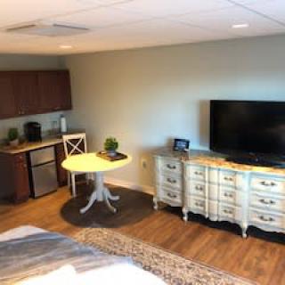 A cozy room featuring a kitchenette, TV on a dresser, and a small round table with a chair.