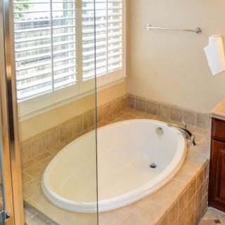 A modern bathroom with an oval bathtub next to a window and glass shower door.