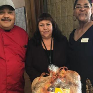 Three individuals posing with a wrapped food gift basket.