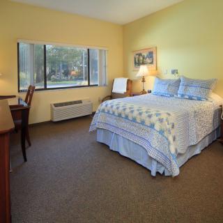 A cozy bedroom with a neatly made bed, a desk, and a large window.