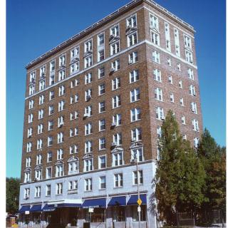 A multi-story brick building with numerous windows and trees in the foreground.