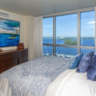 A modern bedroom with a stunning ocean view through large windows, featuring stylish decor and artwork.