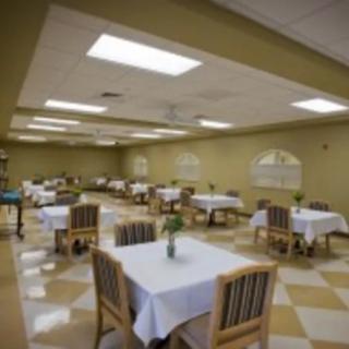 A spacious dining room with neatly arranged tables and chairs, featuring white tablecloths and soft lighting.
