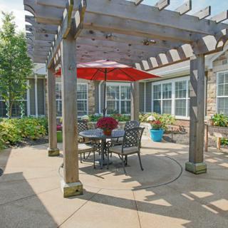 A cozy patio with a pergola, featuring a red umbrella and outdoor seating.