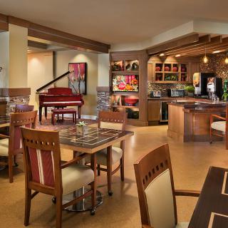 A cozy dining area with a bar and seating, featuring a red piano in the background.