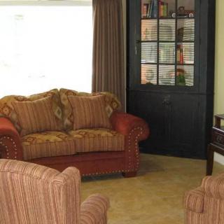 A cozy living room with a sofa and armchairs, a bookshelf, and curtains.