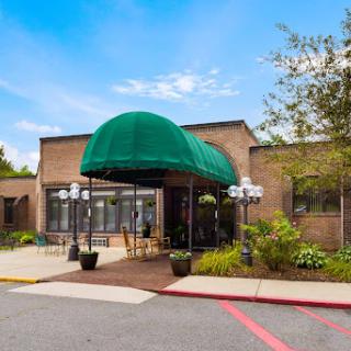 A welcoming entrance with a green awning and outdoor seating, surrounded by lush landscaping.