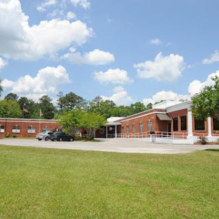 A brick school building surrounded by lush green grass under a clear blue sky.
