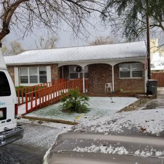 A snow-covered house and yard with a van parked nearby on a winter day.