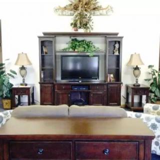 A cozy living room featuring a wooden entertainment center with a television, flanked by lamps and decorative plants.