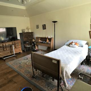 A cozy bedroom with a hospital bed, television, and bookshelf.
