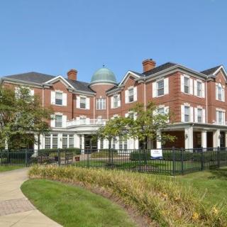 A large, red-brick residential building with a manicured garden and clear blue sky.