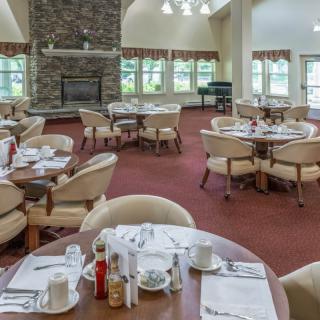 A spacious dining room with neatly arranged tables and chairs, featuring a fireplace and large windows.