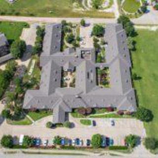 An aerial view of a large building with surrounding greenery and a parking lot.