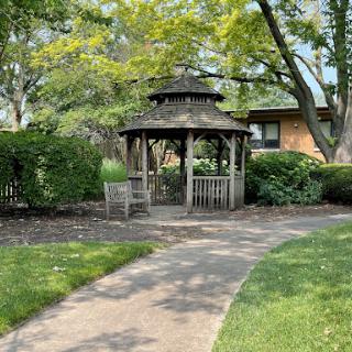 A serene gazebo surrounded by lush greenery and a winding pathway, inviting visitors to relax and enjoy the outdoors.