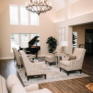 A modern living room featuring elegant furniture and a grand piano under a large chandelier.