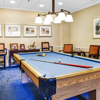 A well-lit game room featuring a pool table with blue felt and surrounding chairs.