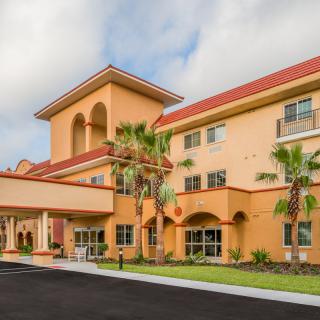 A sunny exterior view of a three-story hotel with palm trees and an inviting entrance.
