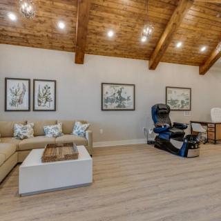A spacious living room features a cozy seating area, massage chair, and modern decor under wooden ceiling beams.