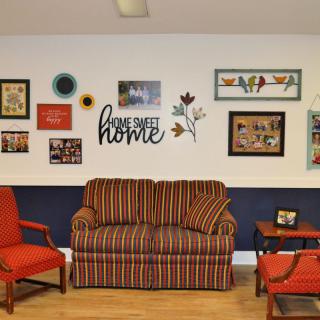 A cozy living room with a striped couch, two red armchairs, and a wall adorned with various artworks.