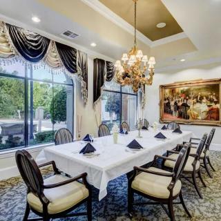 An elegant dining room with a long table set for guests, featuring a chandelier and sophisticated decor.
