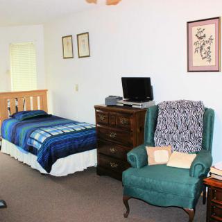A cozy bedroom featuring a single bed, a green armchair, and a dresser with a small television on top.