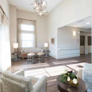 A modern and cozy living room interior featuring elegant furniture, a chandelier, and abundant natural light.