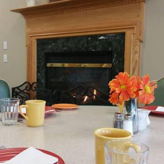 A cozy dining setup with a fireplace in the background, featuring mugs and flowers on the table.