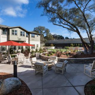 A sunny outdoor patio area with seating and a residential building in the background.