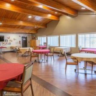 A spacious dining area with round tables and chairs, featuring large windows and wooden beam ceilings.