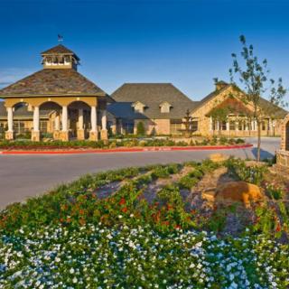A picturesque landscape featuring beautifully manicured gardens in front of a large building with traditional architecture under a clear blue sky.