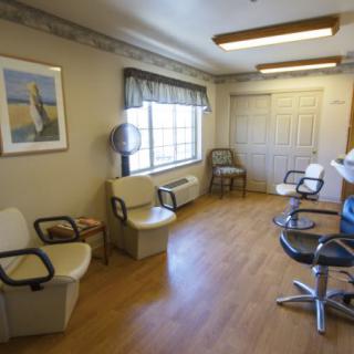 A cozy and well-lit hair salon with chairs for waiting and styling, featuring a wooden floor and a window view.