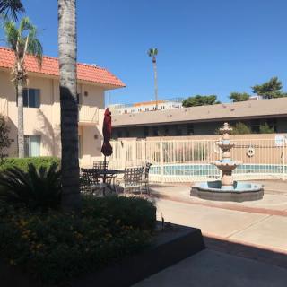 A sunny courtyard of a hotel with a fountain and swimming pool surrounded by patio furniture and palm trees.