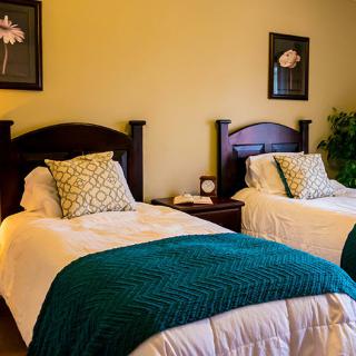 A cozy bedroom with two twin beds, adorned with decorative pillows and teal blankets.