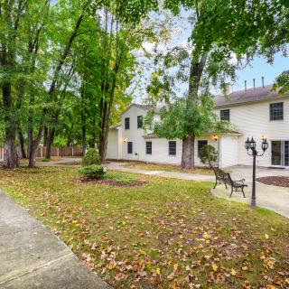 A spacious yard with a residential house surrounded by tall trees and a bench.