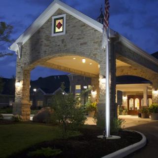 A well-lit entrance of a building at night with landscaping and an American flag.