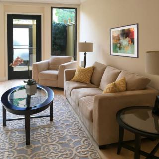 A cozy living room featuring a beige sofa, armchair, and glass coffee table with a patterned rug and modern artwork.