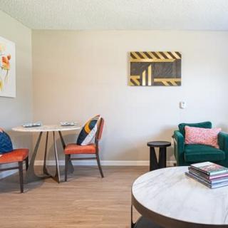 A modern living room with stylish decor, featuring a round table with chairs, a comfortable armchair, colorful cushions, and contemporary wall art.