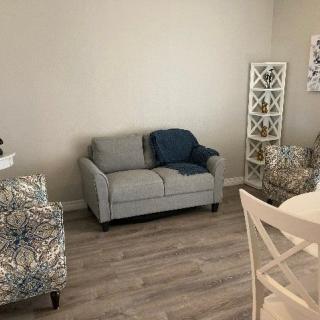 A cozy living room with a gray sofa, patterned armchair, and wooden flooring.