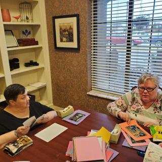 Two individuals engaged in a lively discussion around a table filled with colorful stationery.