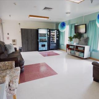 A spacious and well-lit lounge area featuring comfortable seating, a vending machine, and a television.